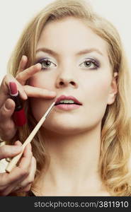 Cosmetic beauty procedures and makeover concept. Makeup artist applying lipstick with accessories tools to woman lips.