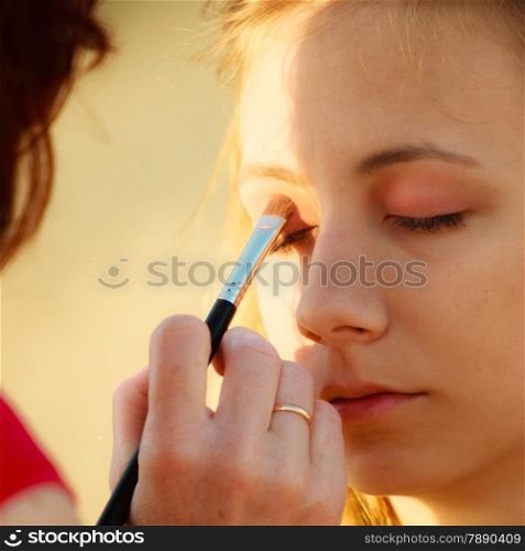 Cosmetic beauty procedures and makeover concept. Makeup artist applying with brush color eyeshadow on female eye.