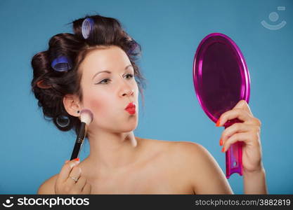 Cosmetic beauty procedures and makeover concept. Woman in hair curlers applying makeup blusher with brush. Girl gets blush on cheekbones, on blue