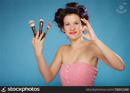 Cosmetic beauty procedures and makeover concept. Woman in hair rollers holding makeup brushes set making ok sign gesture on blue