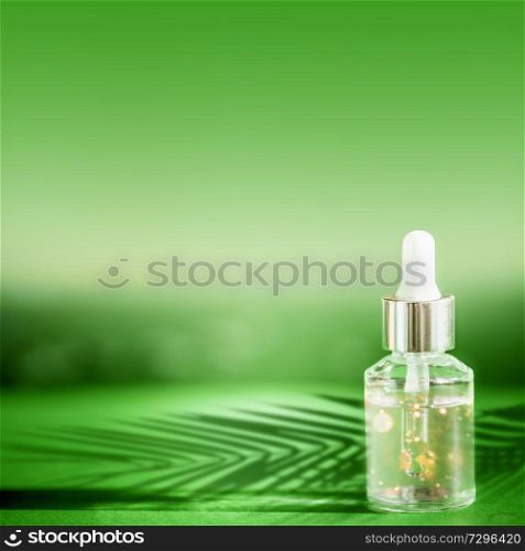 Cosmetic bottle with pipette standing on green table with palm leaves shadow. Facial skin care concept. Natural vegan cosmetic. Serum or skin essential oil. Modern beauty trend.