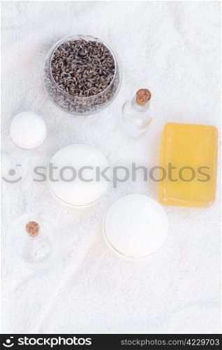 cosmetic containers, bottles, soap and lavender on a white towel
