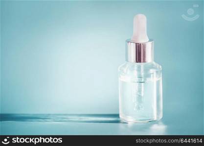Cosmetic or medical bottle with pipette. Transparent liquid product in glass bottle with dropper. Serum skin care on light blue background, front view with copy space. Beauty product