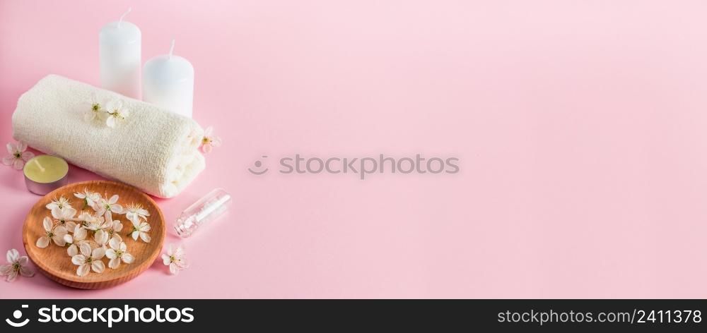 Cosmetic products for spa and aromatherapy. Candles, sea salt, towel and flowers on a pink background. Skin care and beauty concept. Place for your text, banner format. Cosmetic products for spa and aromatherapy. Candles, sea salt, towel and flowers on a pink background. Skin care and beauty concept.