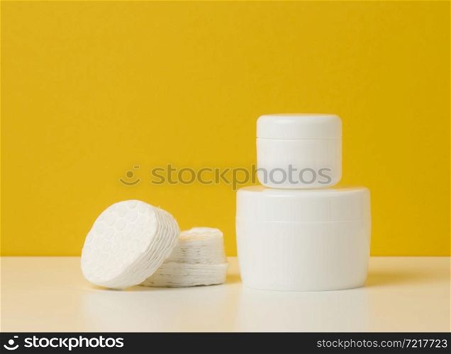 cosmetic products in a white plastic jar with a lid and white cotton pad. Blank for branding products, moisturizer on yellow background
