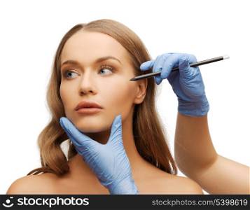 cosmetic surgery concept - woman face and beautician hands with pencil