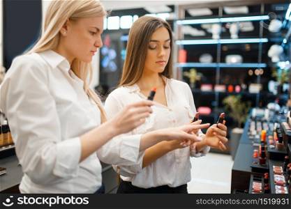 Cosmetician and woman choosing lipstick at the showcase in cosmetics store. Luxury beauty shop salon, female customer and beautician in fashion market. Cosmetician and woman at showcase, cosmetics store