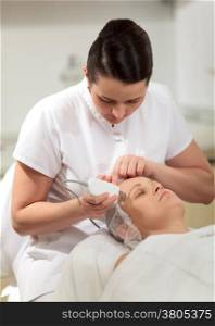Cosmetician and young woman during the seance of ultrasonic facial cleaning