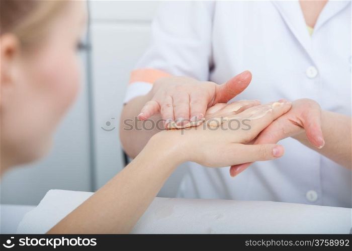 Cosmetician beautician applying orange moisturizing cream balm on hands of female client. Skincare. Woman in healthy beauty spa salon.