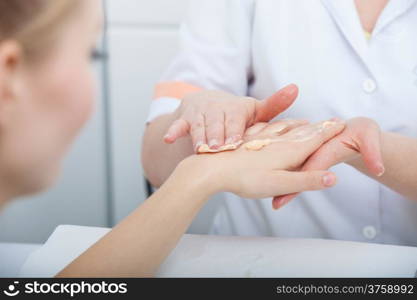 Cosmetician beautician applying orange moisturizing cream balm on hands of female client. Skincare. Woman in healthy beauty spa salon.