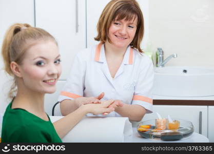 Cosmetician beautician applying orange moisturizing cream balm on hands of female client. Skincare. Woman in healthy beauty spa salon.