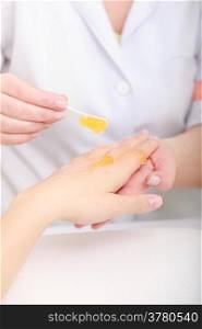 Cosmetician beautician applying orange moisturizing cream balm on hands of female client. Skincare. Woman in healthy beauty spa salon.