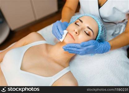 Cosmetician cleans facial skin to female patient. Rejuvenation procedure in beautician salon. Doctor and woman, cosmetic surgery against wrinkles and aging