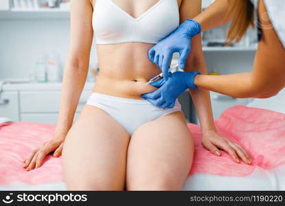 Cosmetician hands in gloves gives botox injection in the stomach to female patient on treatment table. Rejuvenation procedure in beautician salon. Doctor and woman, cosmetic surgery against wrinkles. Cosmetician hands gives botox injection in stomach