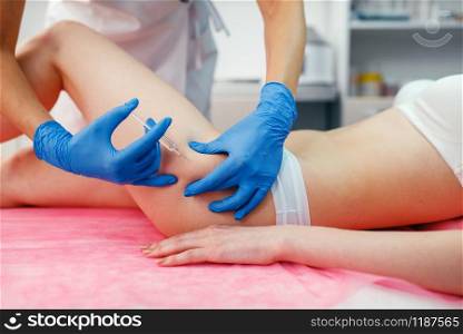 Cosmetician in gloves gives botox injection in the thigh to female patient on treatment table. Rejuvenation procedure in beautician salon. Doctor and woman, cosmetic surgery against wrinkles. Cosmetician gives botox injection in the thigh