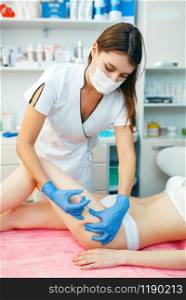 Cosmetician in gloves gives botox injection in the thigh to female patient on treatment table. Rejuvenation procedure in beautician salon. Doctor and woman, cosmetic surgery. Cosmetician gives botox injection in the thigh