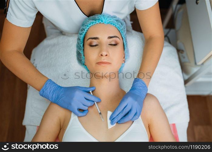 Cosmetician in gloves gives botox injection to female patient on treatment table, top view. Rejuvenation procedure in beautician salon. Doctor and woman, cosmetic surgery against wrinkles