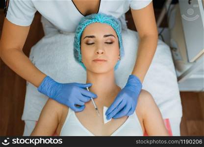 Cosmetician in gloves gives botox injection to female patient on treatment table, top view. Rejuvenation procedure in beautician salon. Doctor and woman, cosmetic surgery against wrinkles