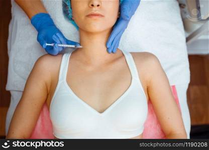 Cosmetician in gloves gives botox injection to female patient on treatment table, top view. Rejuvenation procedure in beautician salon. Doctor and woman, cosmetic surgery against wrinkles. Cosmetician gives botox injection against wrinkles