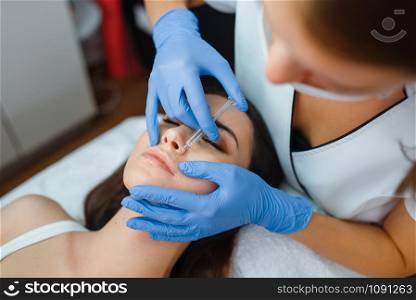 Cosmetician in gloves gives face botox injections to female patient on treatment table. Rejuvenation procedure in beautician salon. Doctor and woman, cosmetic surgery against wrinkles. Cosmetician gives face botox injections to patient