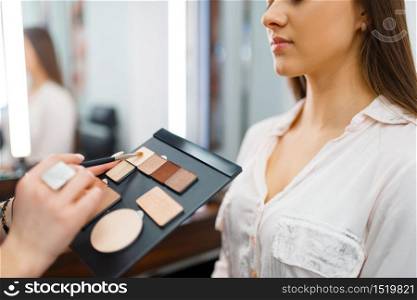 Cosmetician puts shadows on a woman&rsquo;s face in cosmetics store. Luxury beauty shop salon, female customer and beautician in fashion market. Cosmetician puts shadows on a woman&rsquo;s face