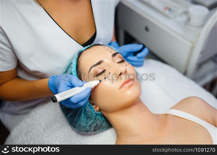 Cosmetician with marker puts dotted lines on female patient face, botox injections preparation. Rejuvenation procedure in beautician salon. Cosmetic surgery against wrinkles and aging