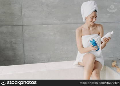 Cosmetics choice  Lady holds cosmetic flacons micellar water or face toner. Gorgeous Caucasian woman, towel-wrapped after bath. Young woman showers at home.