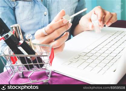 Cosmetics in shopping cart with woman holding lip gloss on hands. Cosmetics in shopping cart with woman holding lip gloss on hands, Online shopping, Beauty concept
