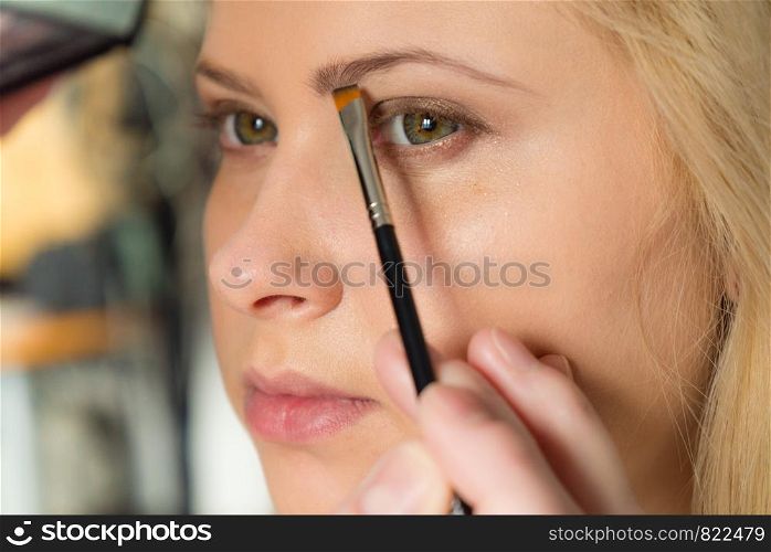 Cosmetics, make up, beauty concept. Woman getting her eyebrows makeup done, applying shadow with professional brush, closeup.. Woman getting her makeup done, eyebrows