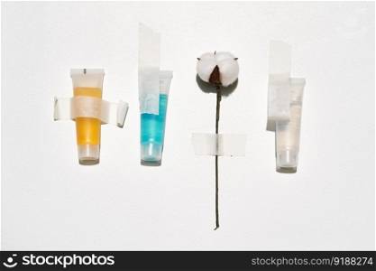 Cosmetics of different colors and a sprig of cotton on a white background with tape.