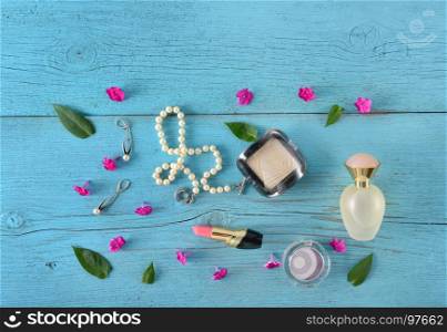 Cosmetics, perfumes and jewelry made of pearls on an old wooden background of blue color. Flat lay, top view. Free space for text.