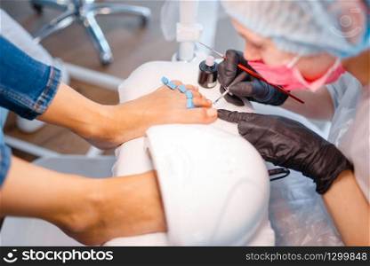 Cosmetologist salon, pedicure, varnish application procedure. Nail care treatment for female client in beauty shop, doctor in gloves works with customer toenails