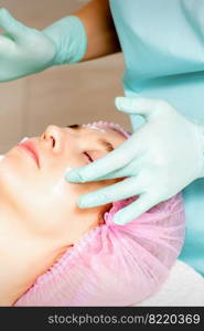 Cosmetologist with gloved hands applies a moisturizing mask with peeling cream on the female face. Facial cosmetology treatment. Procedures for facial care. Cosmetologist with gloved hands applies a moisturizing mask with peeling cream on the female face. Facial cosmetology treatment. Procedures for facial care.