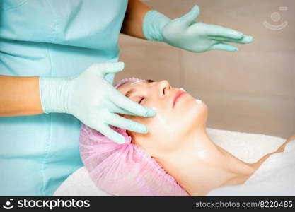 Cosmetologist with gloved hands applies a moisturizing mask with peeling cream on the female face. Facial cosmetology treatment. Procedures for facial care. Cosmetologist with gloved hands applies a moisturizing mask with peeling cream on the female face. Facial cosmetology treatment. Procedures for facial care.