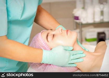 Cosmetologist with gloved hands applies a moisturizing mask with peeling cream on the female face. Facial cosmetology treatment. Procedures for facial care. Cosmetologist with gloved hands applies a moisturizing mask with peeling cream on the female face. Facial cosmetology treatment. Procedures for facial care.