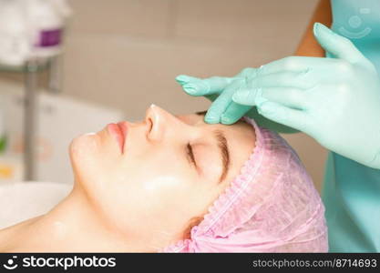 Cosmetologist with gloved hands applies a moisturizing mask with peeling cream on the female face. Facial cosmetology treatment. Procedures for facial care. Cosmetologist with gloved hands applies a moisturizing mask with peeling cream on the female face. Facial cosmetology treatment. Procedures for facial care.