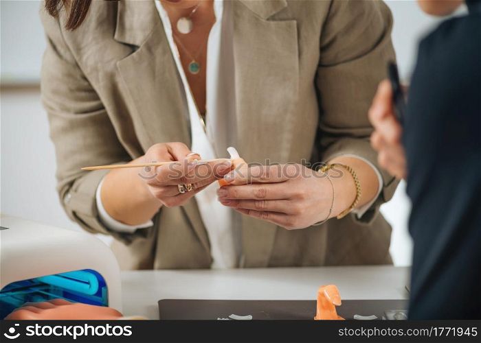 Cosmetology education - program for manicurists and cosmetologists. Beautician practicing for nail technician, pushing the cuticle on mannequin model hand. Cosmetology Education - Program for Manicurists and Cosmetologists