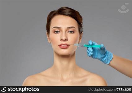 cosmetology, plastic surgery and beauty concept - beautiful young woman and hand with syringe making lifting injection over grey background and snow. beautiful young woman and hand with syringe