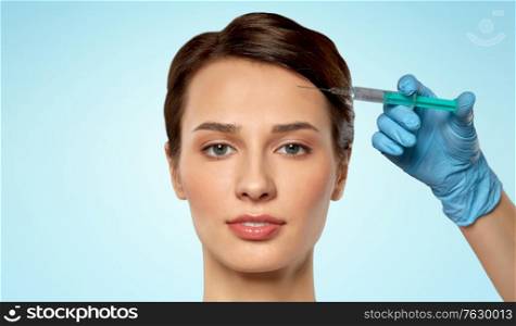 cosmetology, plastic surgery and beauty concept - beautiful young woman and hand with syringe making lifting injection over blue background. beautiful young woman and hand with syringe