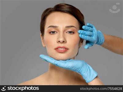 cosmetology, plastic surgery and beauty concept - beautiful young woman face and hands in surgical gloves over grey background and snow. beautiful young woman face and hand in gloves