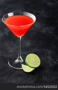 Cosmopolitan cocktail in classic crystal glass with limes on black table background.