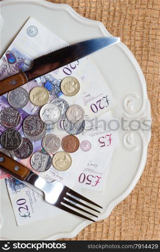 Cost of living, price of food and eating wealth concept. British money on kitchen table, coins and banknotes on plate.