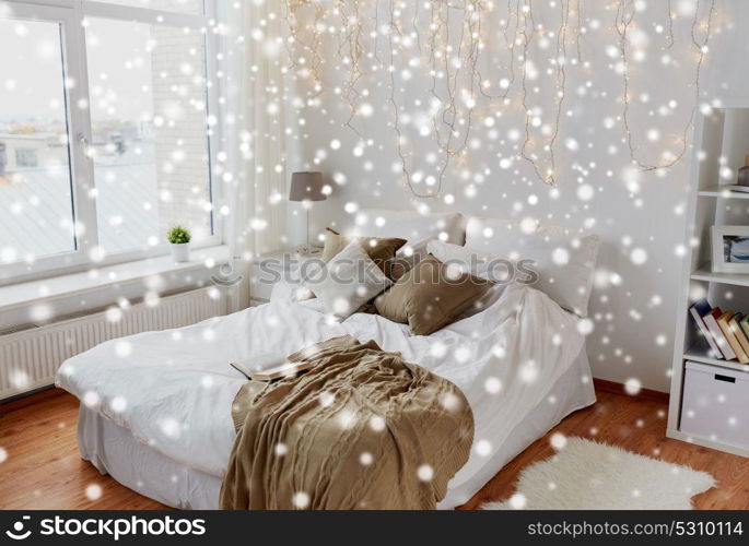 cosy home, interior and holidays concept - cozy bedroom with bed and christmas garland lights over snow. bedroom with bed and christmas garland at home