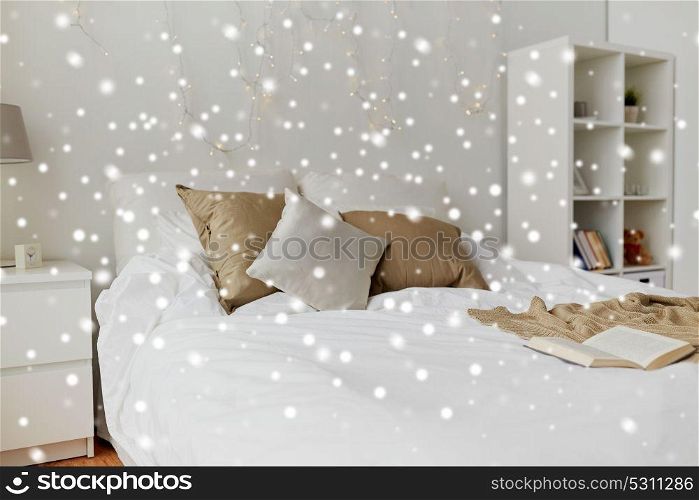 cosy home, interior and holidays concept - cozy bedroom with bed and christmas garland lights over snow. bedroom with bed and christmas garland at home