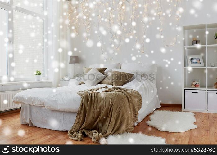 cosy home, interior and holidays concept - cozy bedroom with bed and christmas garland lights over snow. bedroom with bed and christmas garland at home