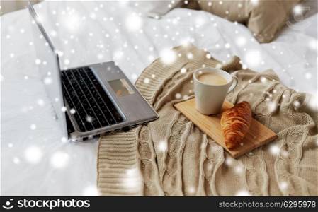 cosy home, interior and winter concept - cozy bedroom with laptop computer, coffee cup and croissant on bed over snow. laptop, coffee and croissant on bed at cozy home
