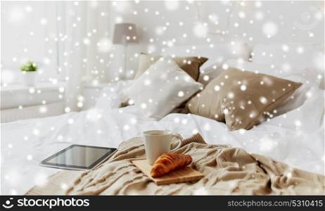 cosy home, morning and winter concept - tablet pc computer, coffee cup and croissant on bed over snow. tablet pc, coffee and croissant on bed at home