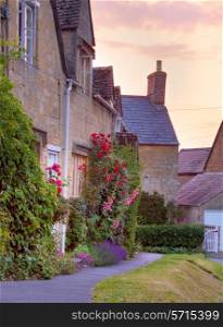 Cotswold cottages with hollyhocks and roses at sunset, Mickleton near Chipping Campden, Gloucestershire, England.