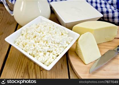 Cottage cheese and sour cream in bowls, milk in glass jug, cheese, knife, napkin on a wooden boards background