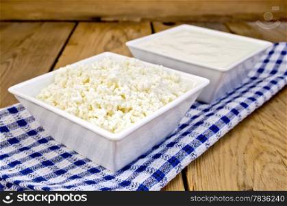 Cottage cheese and sour cream in white square bowls on a blue checkered napkin on wooden board background